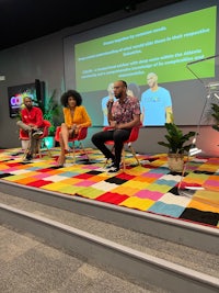 a group of people sitting on a stage in front of a colorful carpet